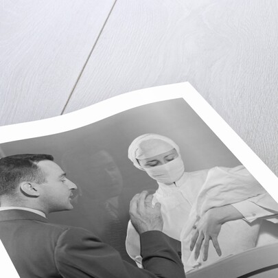 Female nurse holding infant up to father at nursery window by Anonymous