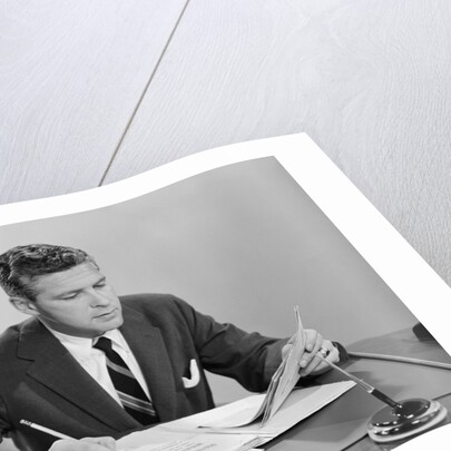 Businessman at desk looking over files papers making notes with pencil by Anonymous