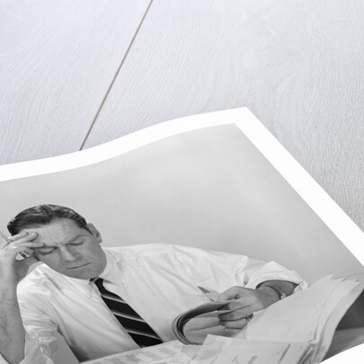 Businessman desk full papers hand to forehead serious expression by Anonymous