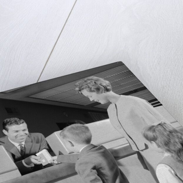 Mother two children boy handing banking deposit to male bank teller by Anonymous