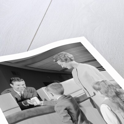 Mother two children boy handing banking deposit to male bank teller by Anonymous