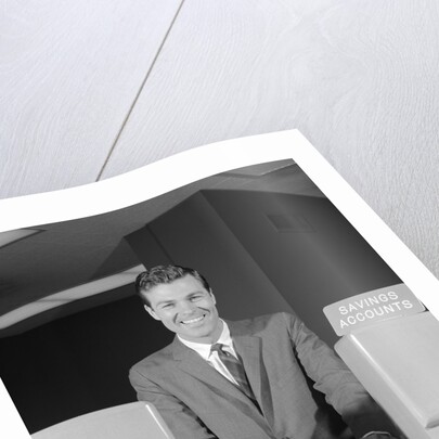 Smiling man bank teller savings accounts sign on counter by Anonymous