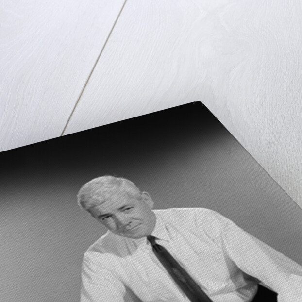 Middle aged man shirt sleeves rolled up standing blueprints on table by Anonymous