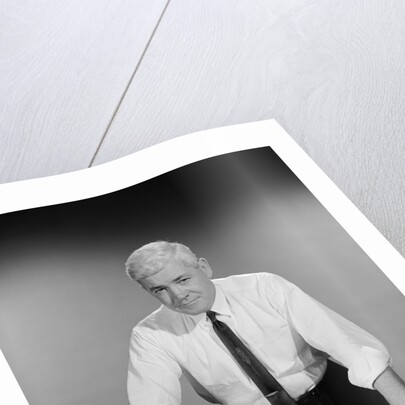 Middle aged man shirt sleeves rolled up standing blueprints on table by Anonymous