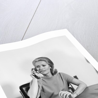 Blond businesswoman talking on telephone sitting at desk by Anonymous
