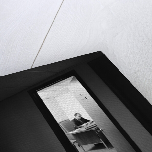 Executive businessman at desk seen working late through door ajar by Anonymous