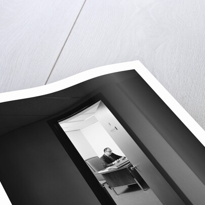 Executive businessman at desk seen working late through door ajar by Anonymous