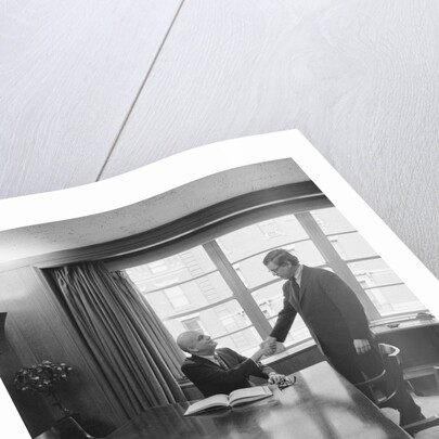 Two men one seated shaking hands long wooden conference table by Anonymous