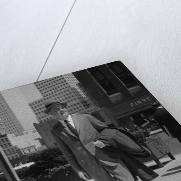 Businessman wearing suit hat carrying top coat standing on city street by Anonymous