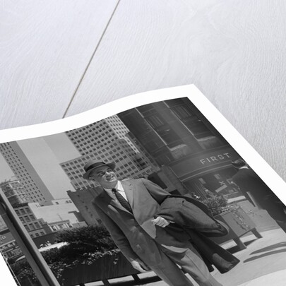 Businessman wearing suit hat carrying top coat standing on city street by Anonymous