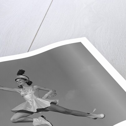 Woman majorette holding baton wearing short skirt uniform jumping into the air by Anonymous