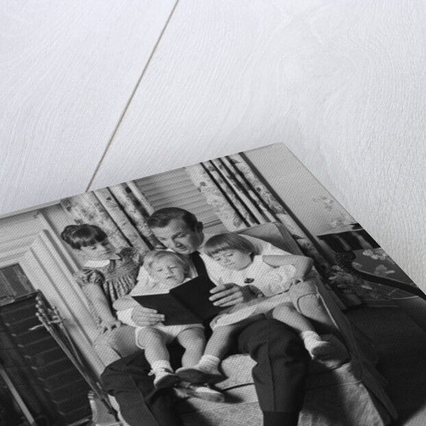 Man father sitting in chair with three children reading book by Anonymous