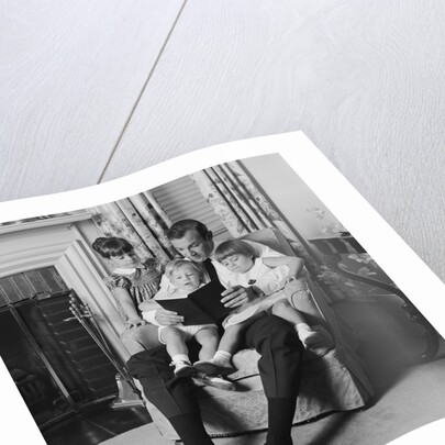Man father sitting in chair with three children reading book by Anonymous