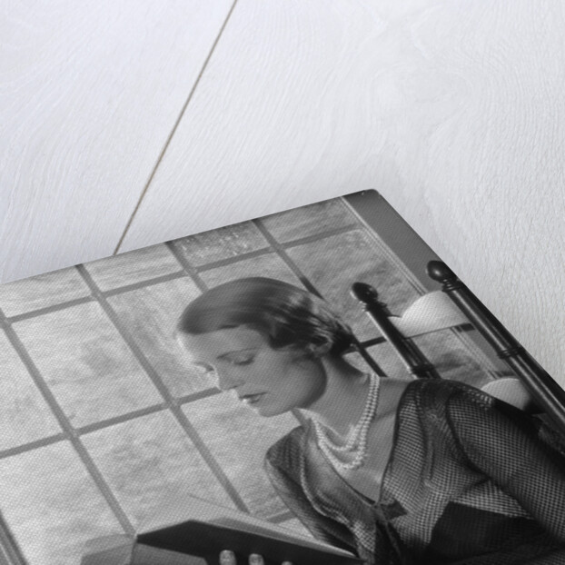 Elegant woman wearing pearls sitting by window reading book by Anonymous