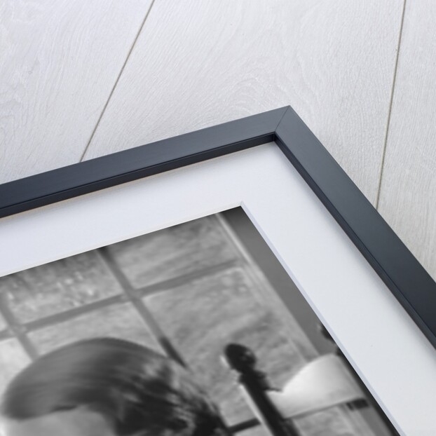 Elegant woman wearing pearls sitting by window reading book by Anonymous