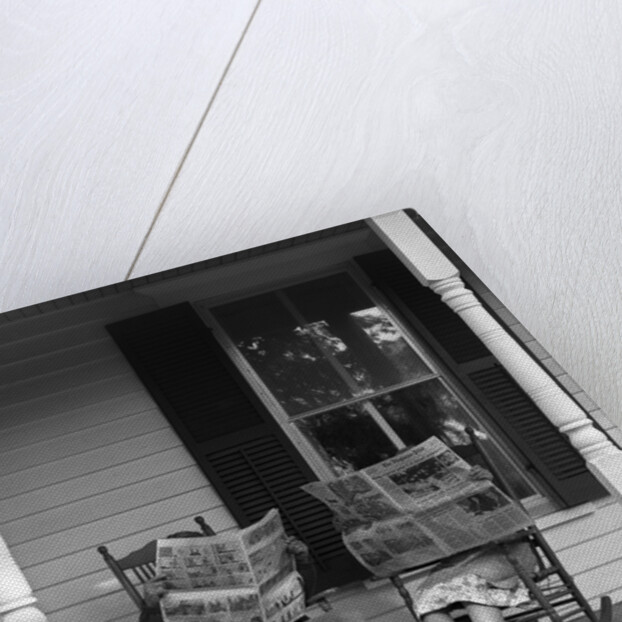 Couple man woman sitting on porch in rocking chairs holding newspapers up hiding their faces by Anonymous