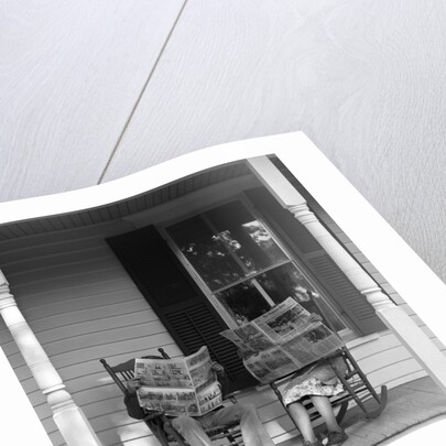 Couple man woman sitting on porch in rocking chairs holding newspapers up hiding their faces by Anonymous