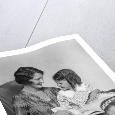 Mother & daughter smiling sitting in chair reading book by Anonymous