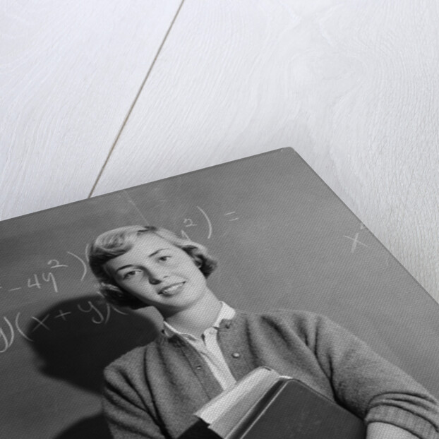 Teenage girl holding school books standing in front of blackboard by Anonymous
