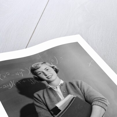 Teenage girl holding school books standing in front of blackboard by Anonymous