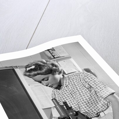 Teen girl writing notes working with microscope in science classroom by Anonymous