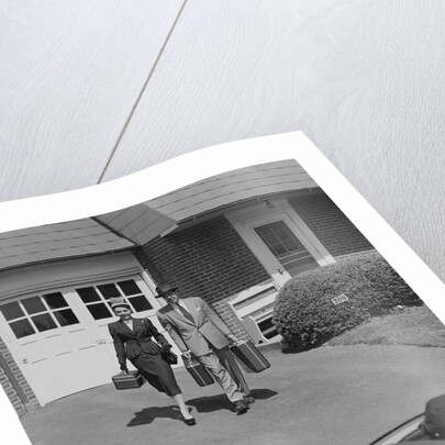 Couple carrying luggage walking towards convertible car in driveway by Anonymous