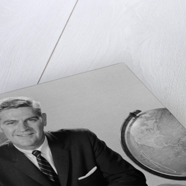 Smiling man sitting at desk with earth globe by Anonymous
