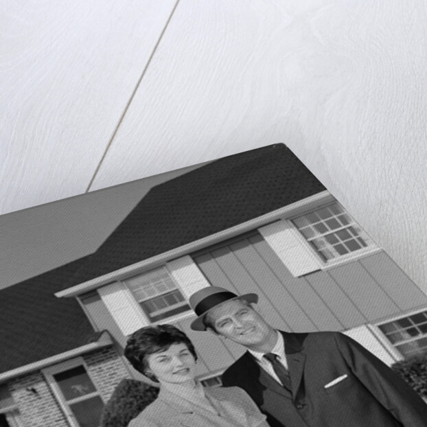 Couple smiling man and woman standing before suburban house by Anonymous