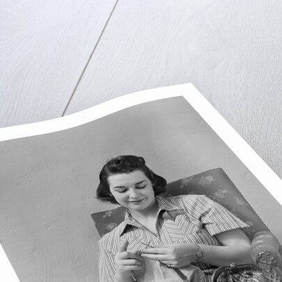 Brunette woman knitting sitting in armchair by Anonymous
