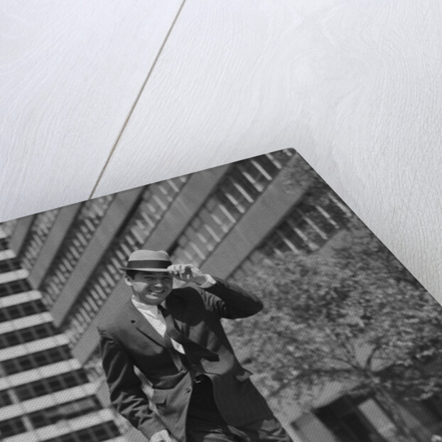 Businessman carrying briefcase holding his hat on running down urban sidewalk by Anonymous