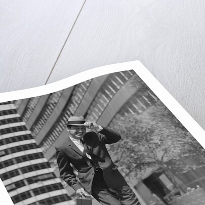 Businessman carrying briefcase holding his hat on running down urban sidewalk by Anonymous