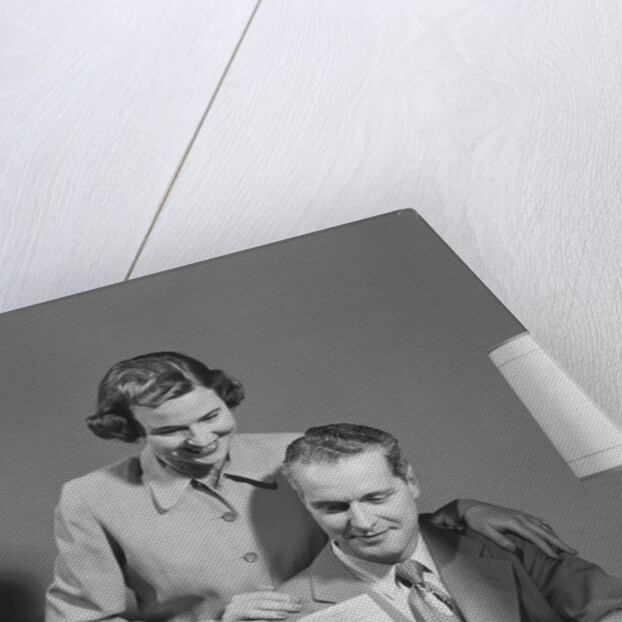 Couple man seated at desk holding paper woman standing looking over his shoulder smiling happy by Anonymous