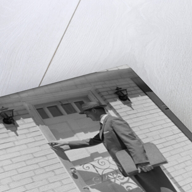 Salesman wearing suit tie hat carrying briefcase ringing suburban house doorbell by Anonymous