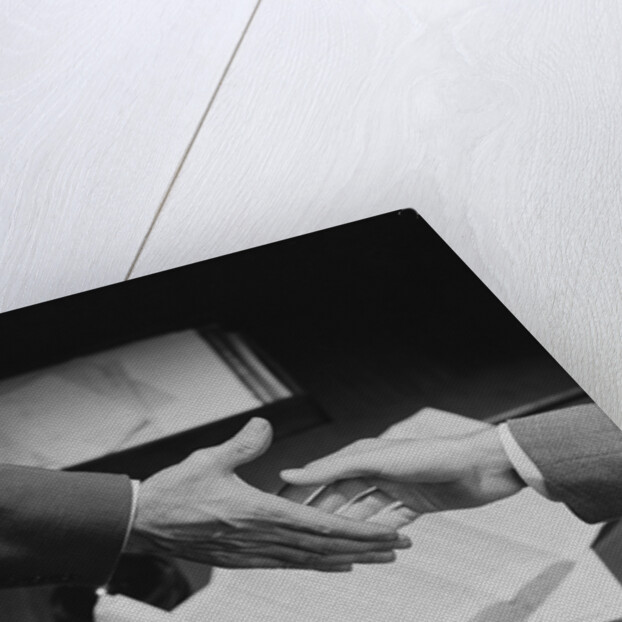 Close-up two male hands about to shake over desk with papers and telephone by Anonymous