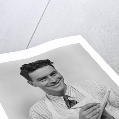 Smiling curly hair man wearing apron taking order with pencil and note pad by Anonymous