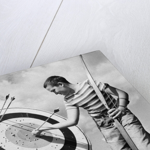 1960s boy jeans striped t-shirt holding bow & pulling arrow out of target bull's-eye by Anonymous