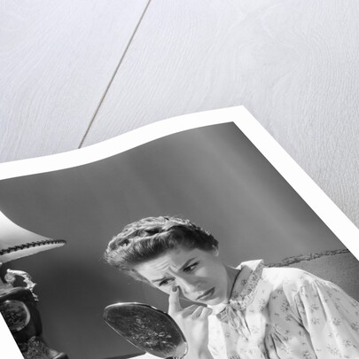 1950s 1960s woman in nightgown holding mirror look at eye wrinkles aging beauty cosmetic serious concerned expression by Anonymous