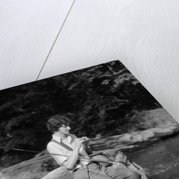 1920s 1930s woman sitting on rock by side of stream wearing waders putting fly on tippet by Anonymous