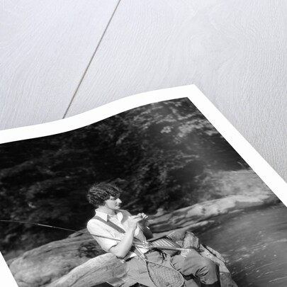 1920s 1930s woman sitting on rock by side of stream wearing waders putting fly on tippet by Anonymous