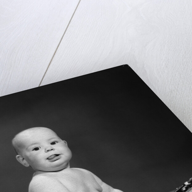 1950s 1960s baby in diaper sticking out tongue holding glasses sitting before adding machine looking at camera by Anonymous