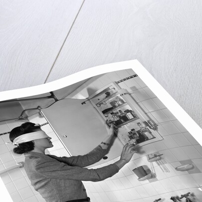 1940s woman wearing blindfold reaching into bathroom medicine cabinet by Anonymous