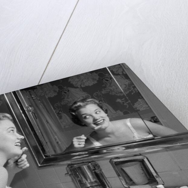 1950s smiling woman looking into bathroom mirror brushing teeth by Anonymous