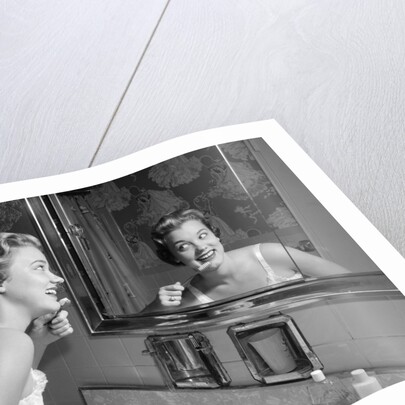 1950s smiling woman looking into bathroom mirror brushing teeth by Anonymous