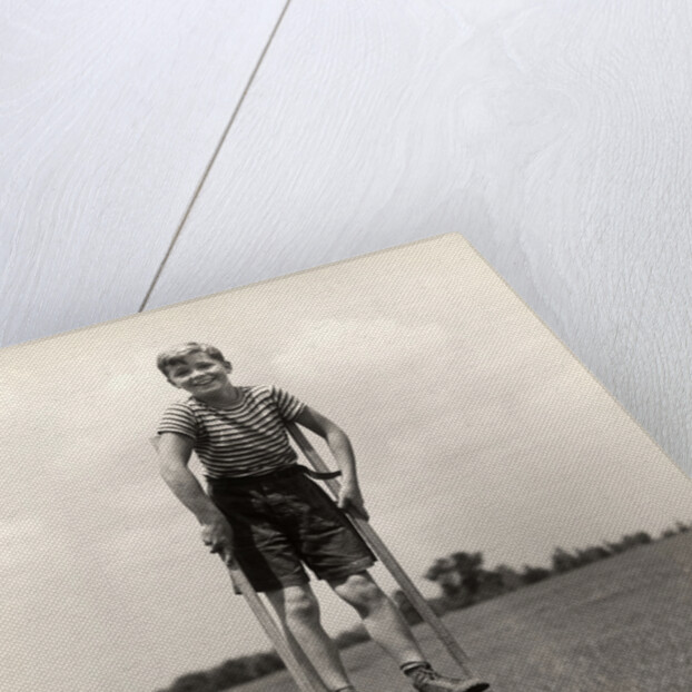 1930s 1940s smiling happy boy wearing striped shirt & short pants walking on pair of stilts looking at camera by Anonymous