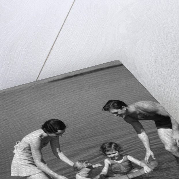 1930s family father mother daughter son with rubber inner tube wading in seashore water by Anonymous