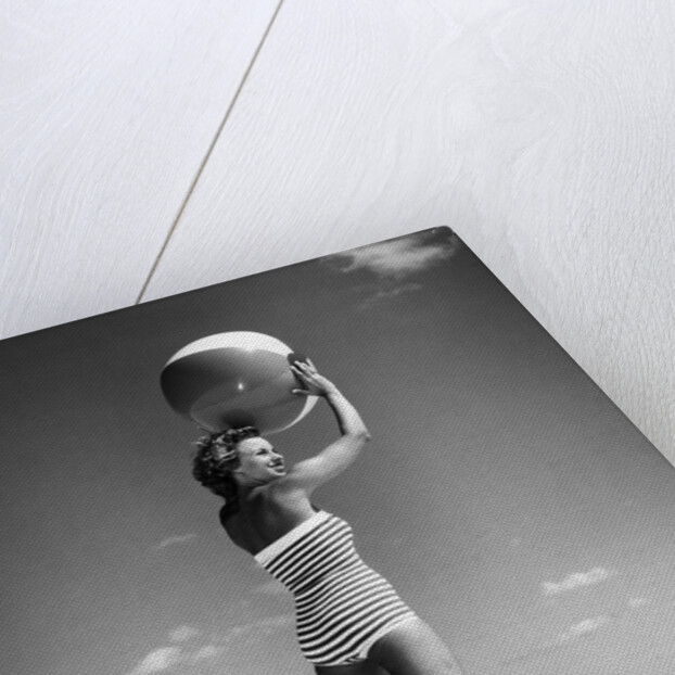 1960s woman in stripes swim suit bathing holding beach ball standing on tip toes by Anonymous