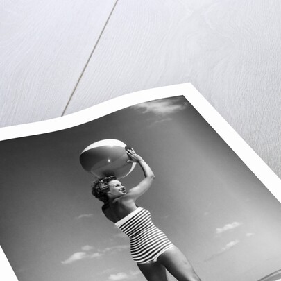 1960s woman in stripes swim suit bathing holding beach ball standing on tip toes by Anonymous