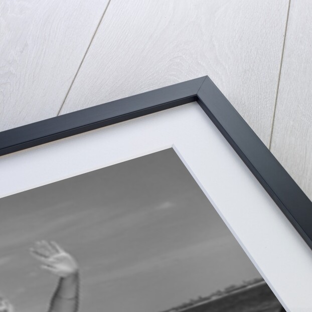 1960s smiling blond teenage girl sitting on rocky shore holding a beach ball waving looking at camera by Anonymous