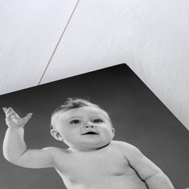 1950s portrait of baby sitting one arm raised waving by Anonymous
