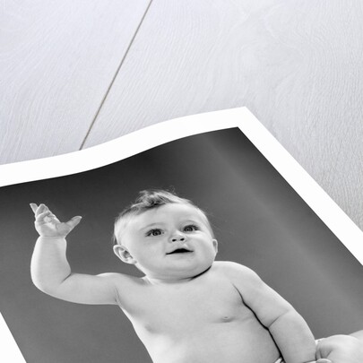 1950s portrait of baby sitting one arm raised waving by Anonymous